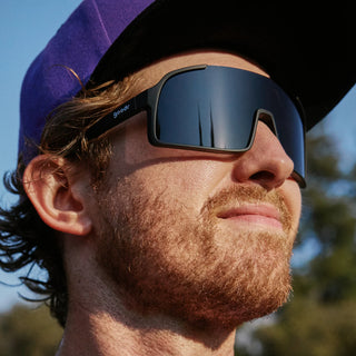 Man wearing goodr sunglasses and a purple cap outdoors