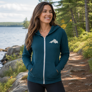 Woman wearing a teal hoodie with a Lake Superior logo by a lakeside forest