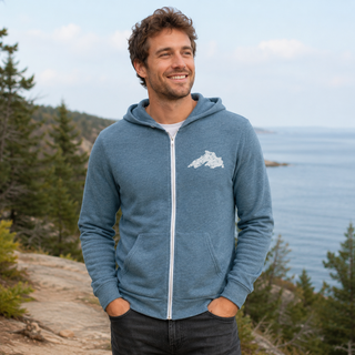 Man wearing a blue hoodie with a Lake Superior logo standing by a scenic lakeside.