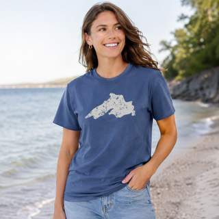 Woman wearing a blue t-shirt with a graphic design standing on a beach. AdventureUs Lake Superior Vintage Print T Shirt - Lifestyle