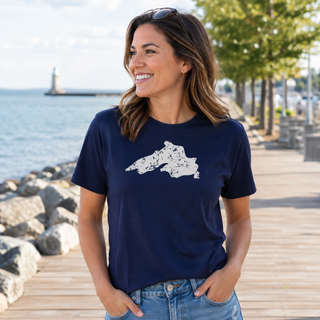 Woman wearing a navy blue t-shirt with a Lake Superior graphic design, standing on a wooden boardwalk by the water.