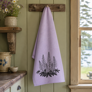 Purple towel with floral design hanging on a wooden hook against a green wall.