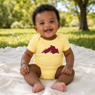 Baby wearing a yellow onesie with a red Lake Superior graphic, sitting on a blanket outdoors.