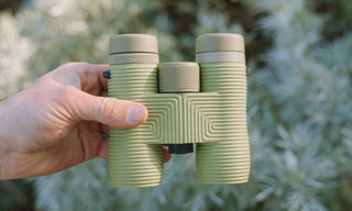 Hand holding a green binoculars against a blurred natural background