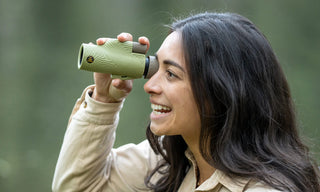 Woman using a green nocs monocular in a forest setting