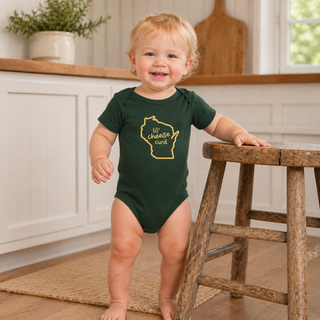 Child wearing a green onesie with a yellow graphic in a kitchen setting
