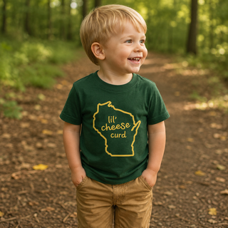 Child wearing a green t-shirt with a yellow lil cheese curd and Wisconsin graphic and text, standing in a forest.