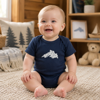 Baby wearing a navy blue onesie with a white design, sitting on a carpeted floor.