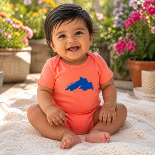 Baby wearing an orange onesie with a blue graphic, sitting on a blanket with flowers in the background