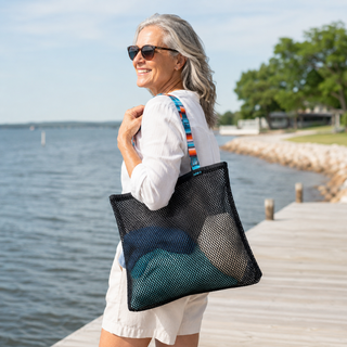 Woman holding a black mesh tote bag by a body of water