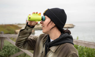 Person using binoculars by a body of water